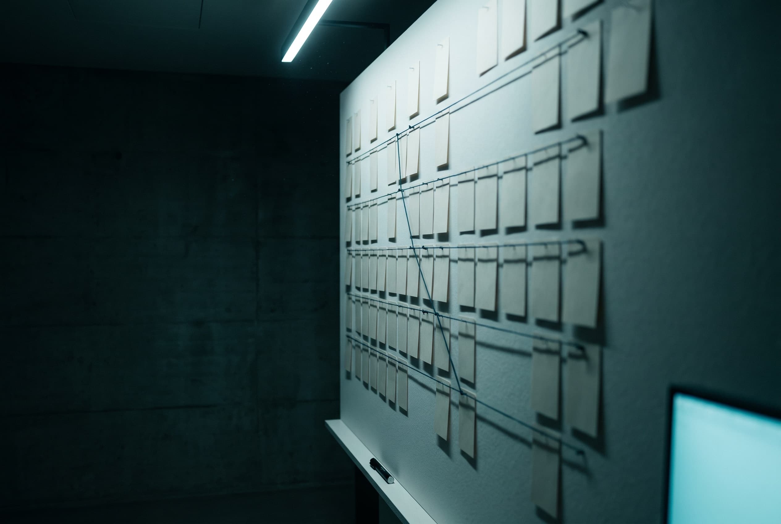 Mur de projet dans un studio genevois, grille de fiches reliées par des fils tendus.