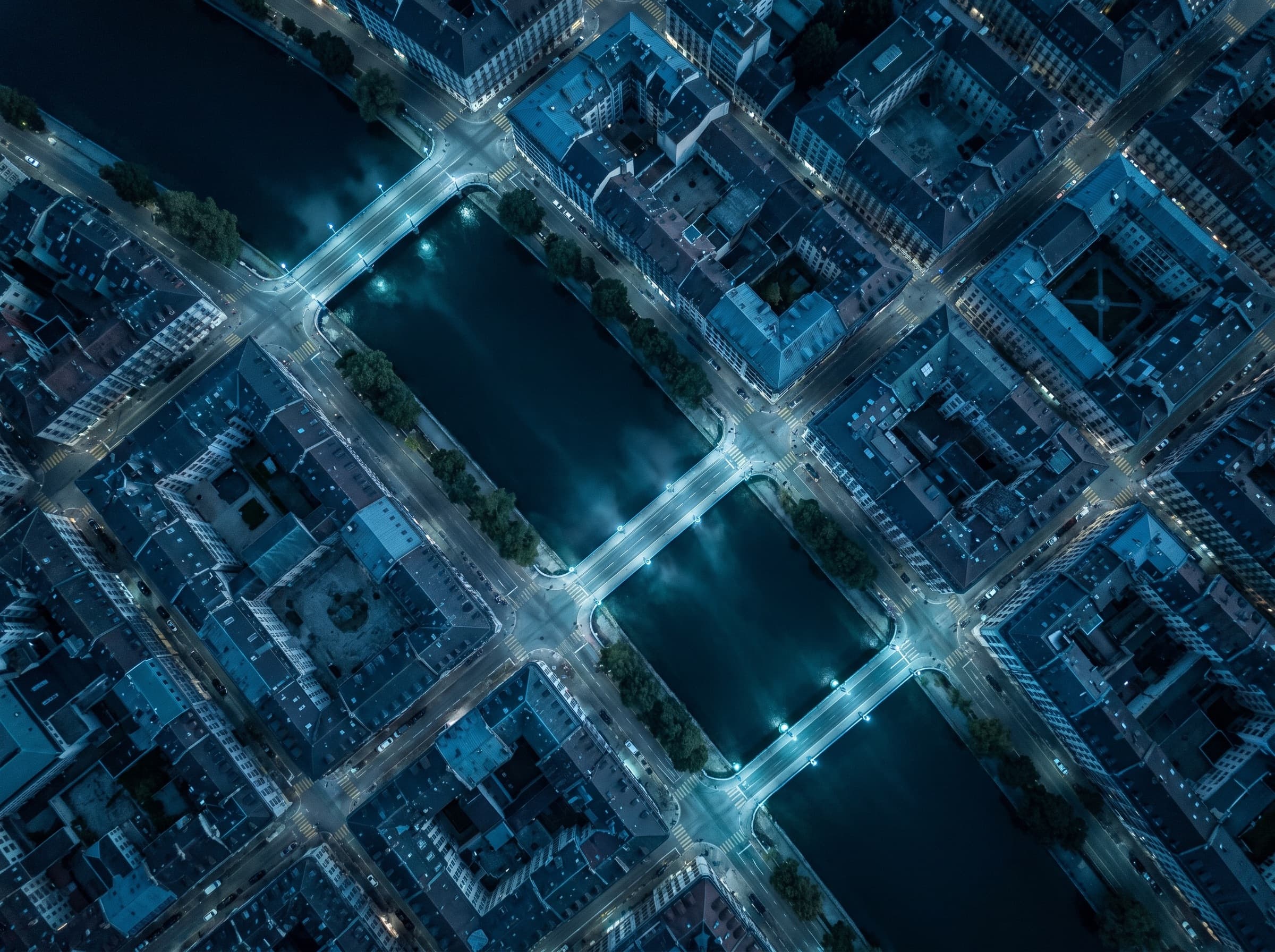 Vue aérienne verticale du centre de Genève à l'heure bleue, le Rhône traversant la trame des toits.